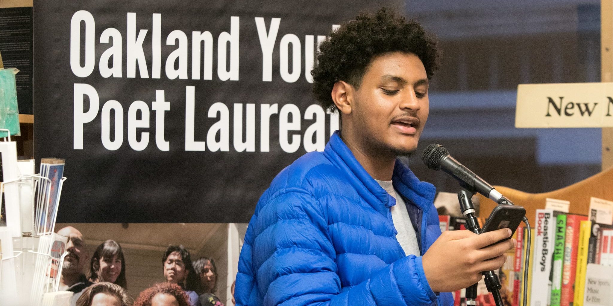 young person is reading a poem from their cellphone into a microphone for a performance in a book store