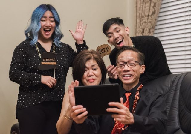 A family smiles and waves at friends and relatives on a tablet